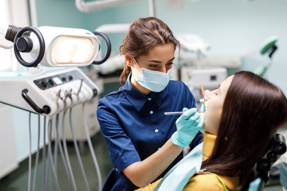 The beautiful young woman is at the dentist. She sits in the dentist's chair and the dentist carefully examines the patient's teeth. The dentist consults a patient sitting in a chair at the clinic