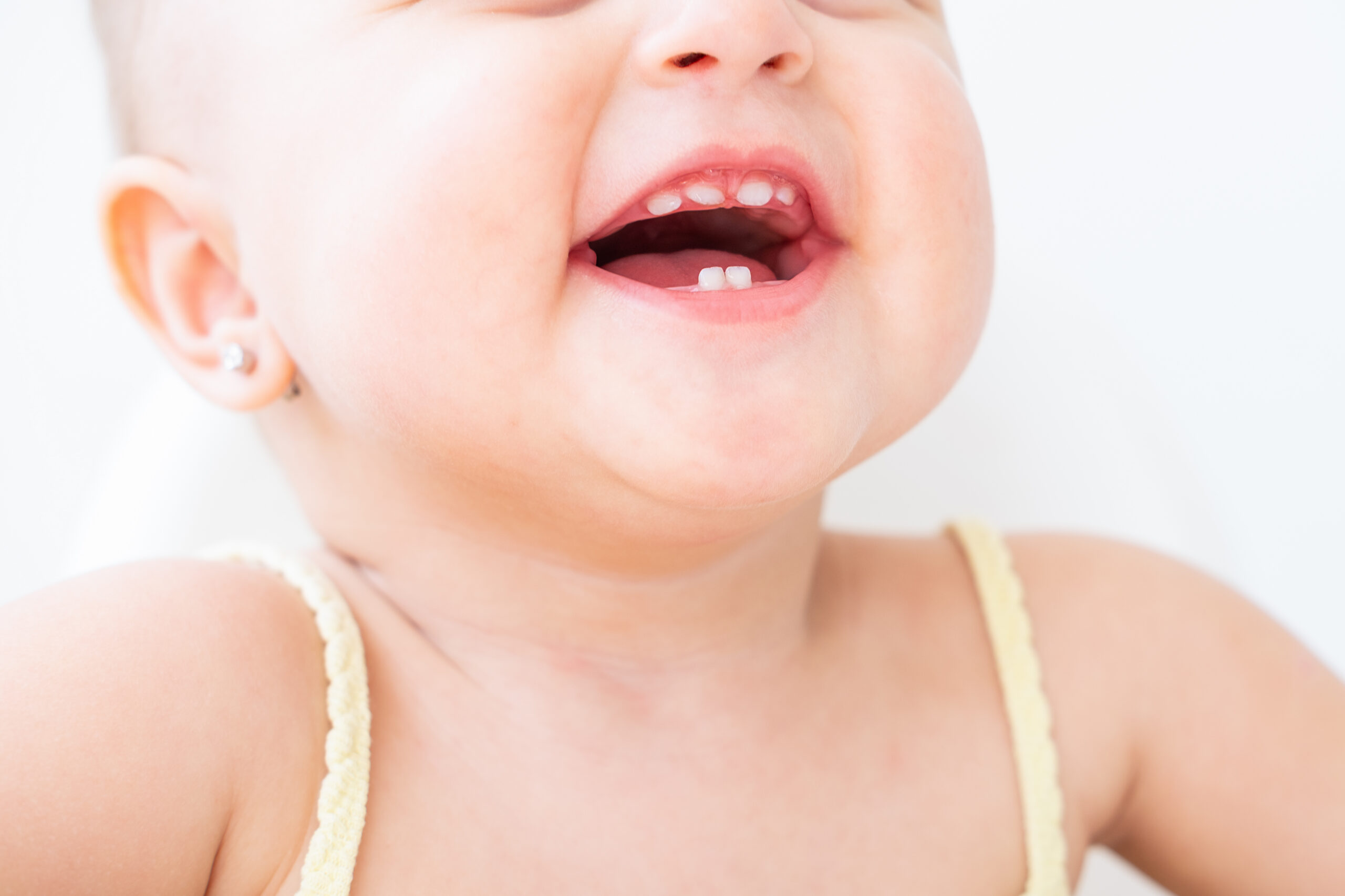Smiling baby showing first baby teeth, with two lower front teeth and four upper front teeth coming through