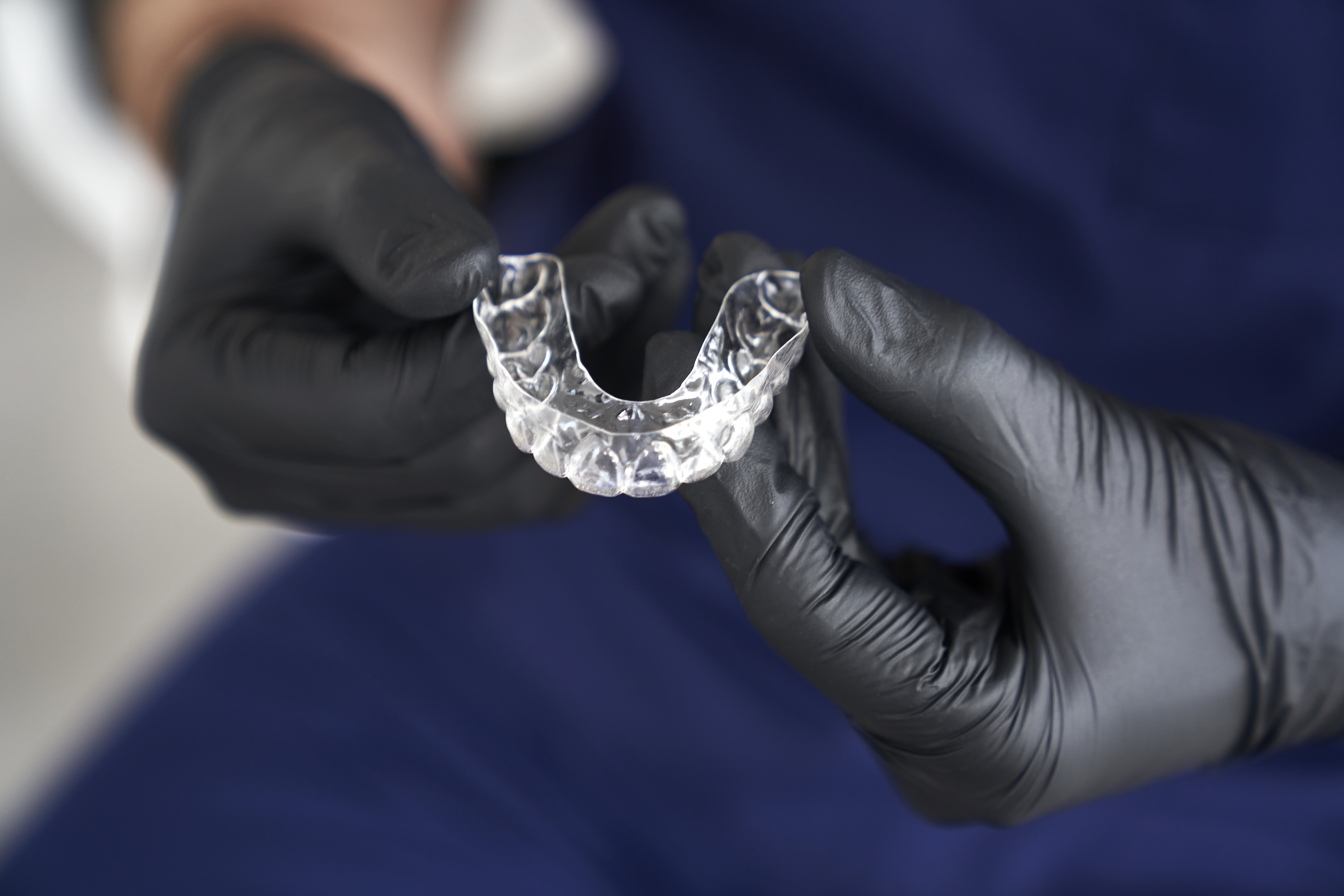 Dentist in black gloves holding a clear custom mouth guard for teeth grinding