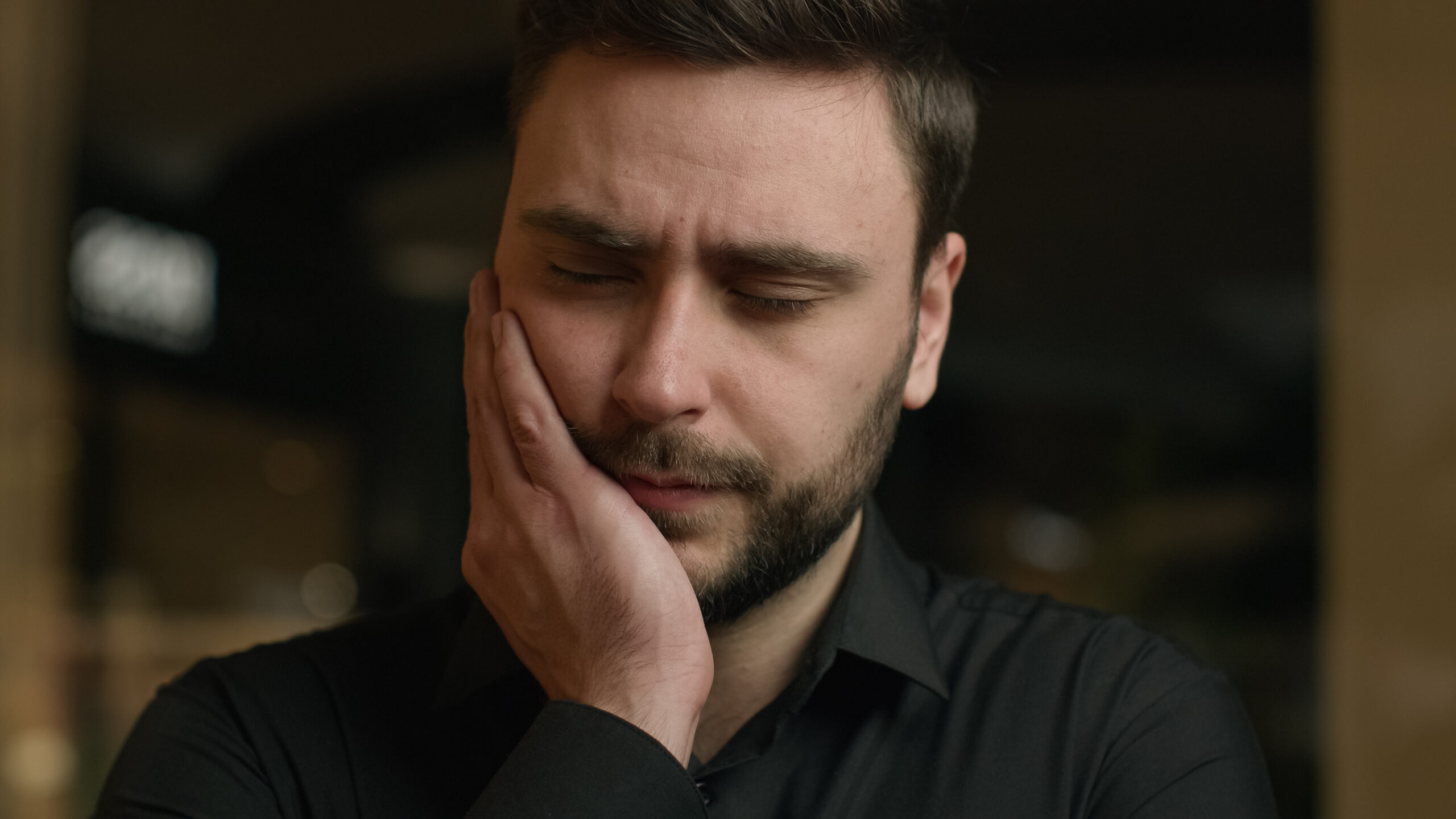 Man with closed eyes holding his cheek in pain, looking for toothache relief