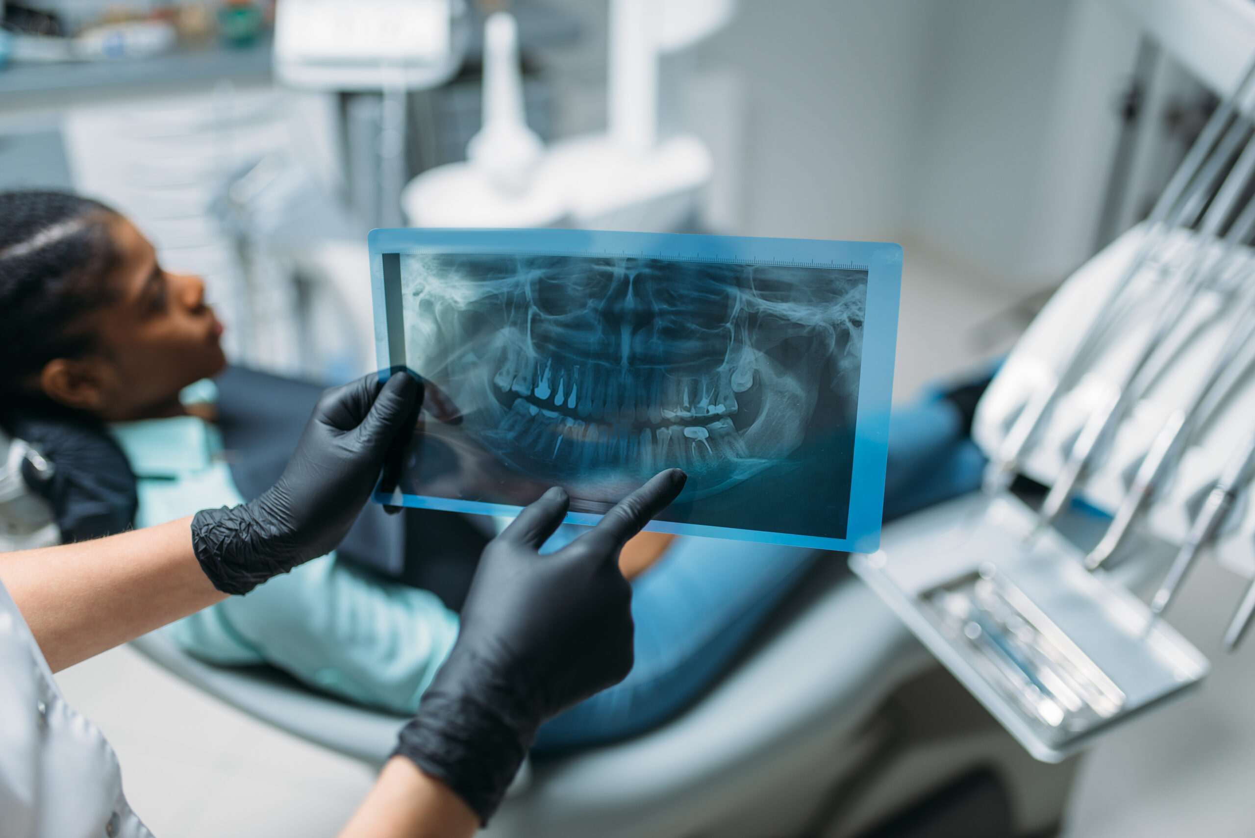 Dentist in black gloves holding a panoramic dental x-ray while a patient reclines in the dental chair