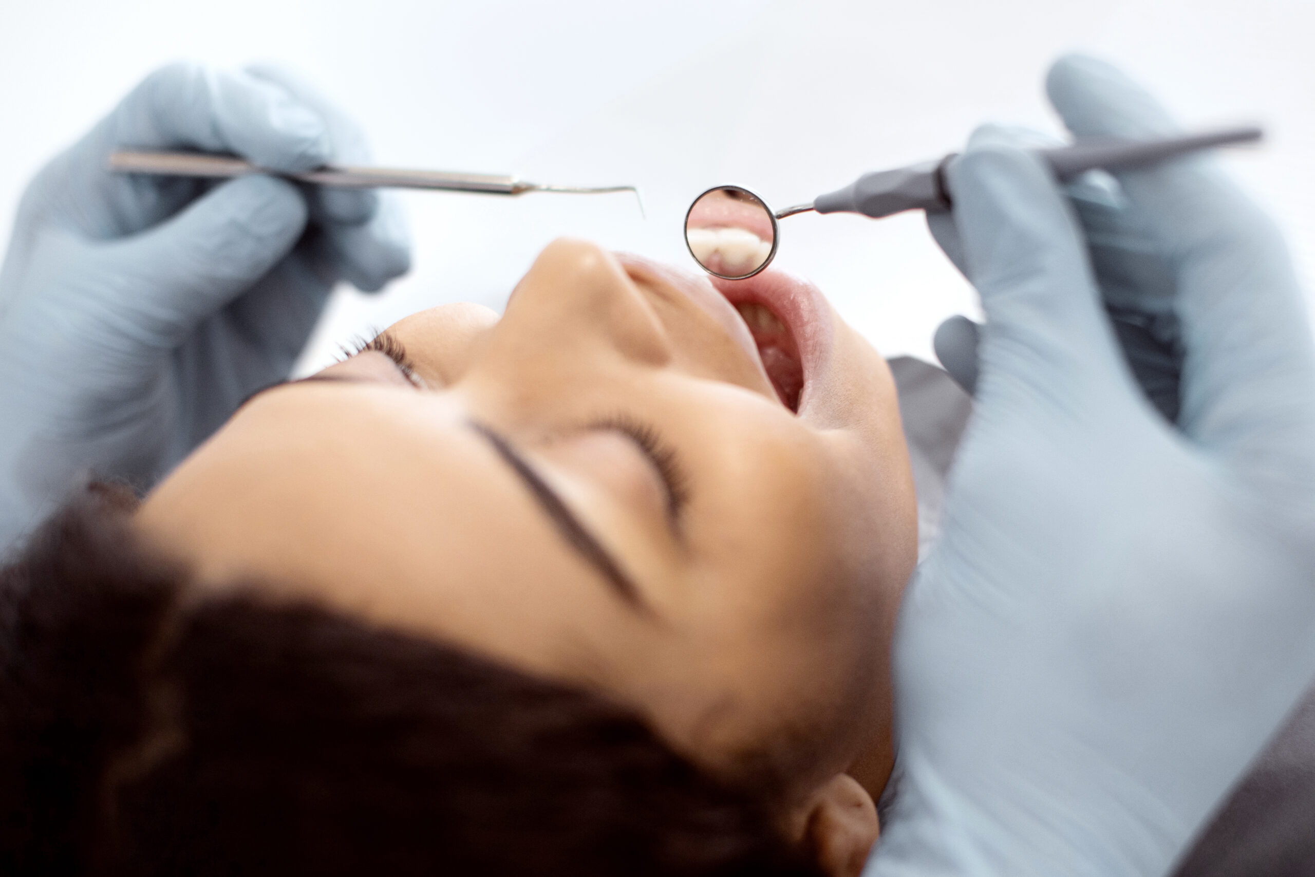Dentist examining a woman’s teeth with a dental mirror and probe during an emergency dental appointment